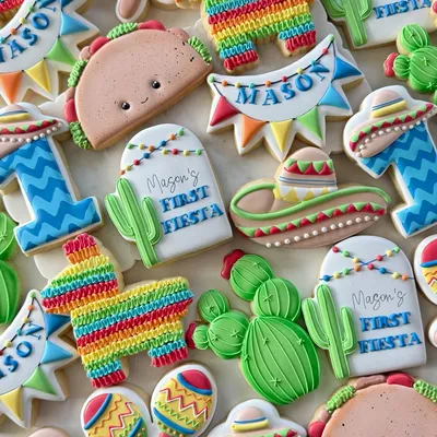 Fiesta-themed first birthday cookie set for "Mason" with a piñata, cactus, sombrero, maracas, and a smiling taco in bright red, yellow, and green.
