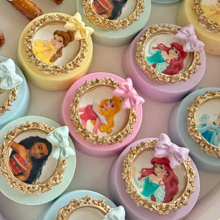 Chocolate-covered Oreos dipped in pastel colors, each topped with a gold-framed Disney princess portrait.