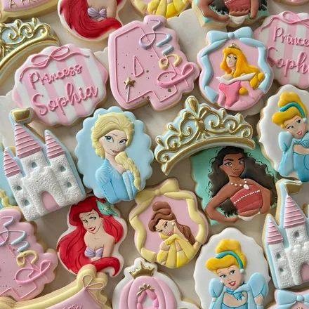 Disney princess-themed 4th birthday cookie set for "Princess Sophia" with hand-painted portraits of Ariel, Belle, Moana, Elsa, Aurora, and Cinderella, a castle, tiara, and pumpkin carriage in pink and gold.