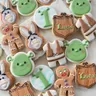 Shrek-themed first birthday cookie set for "Luca" with Shrek and Donkey faces, a gingerbread man, ogre ears, and a wood-shield name plaque in green and brown.