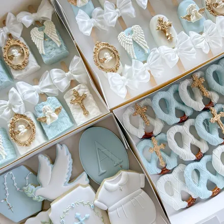 Small party package with christening-themed treats: angel-wing and gold-cross cake pops, a dove cookie, and a "God Bless Asher" plaque in blue, white, and gold.