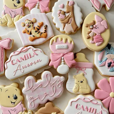 Winnie the Pooh-themed baby shower cookie set for "Camila Aurora" with Pooh, Tigger, Eeyore, and Kanga and Roo, a honey pot, and "Baby Girl" lettering in soft pink and yellow.